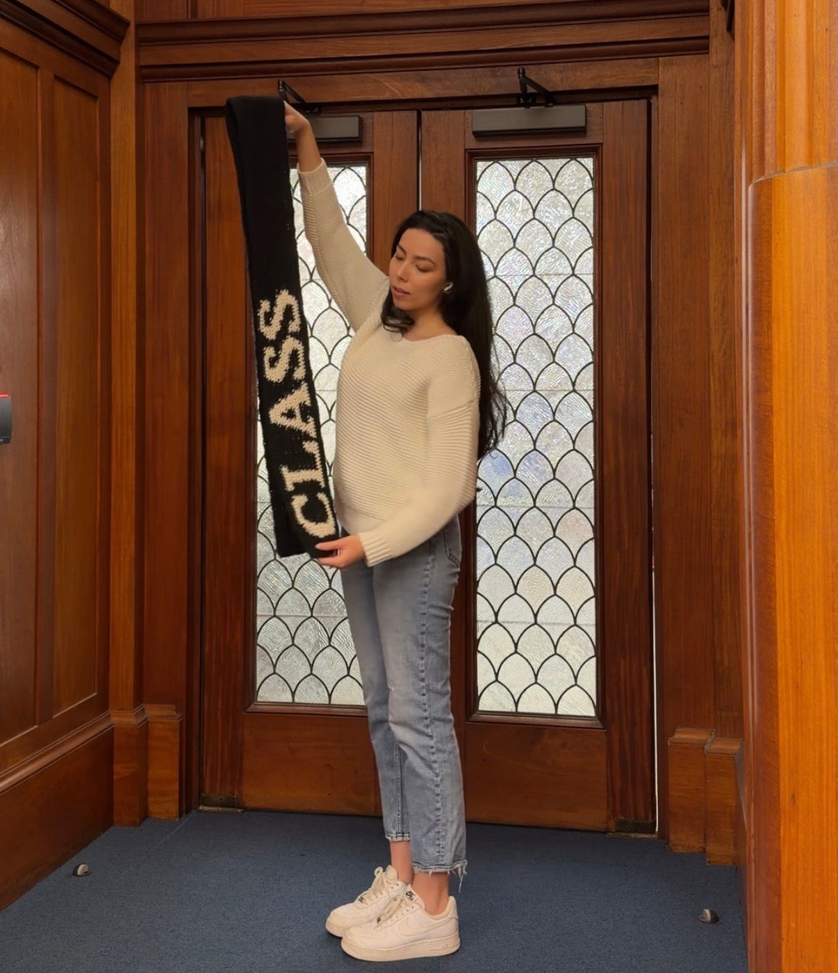 Person holding a 'Class of 2023' banner in a room with wooden walls and stained glass windows.