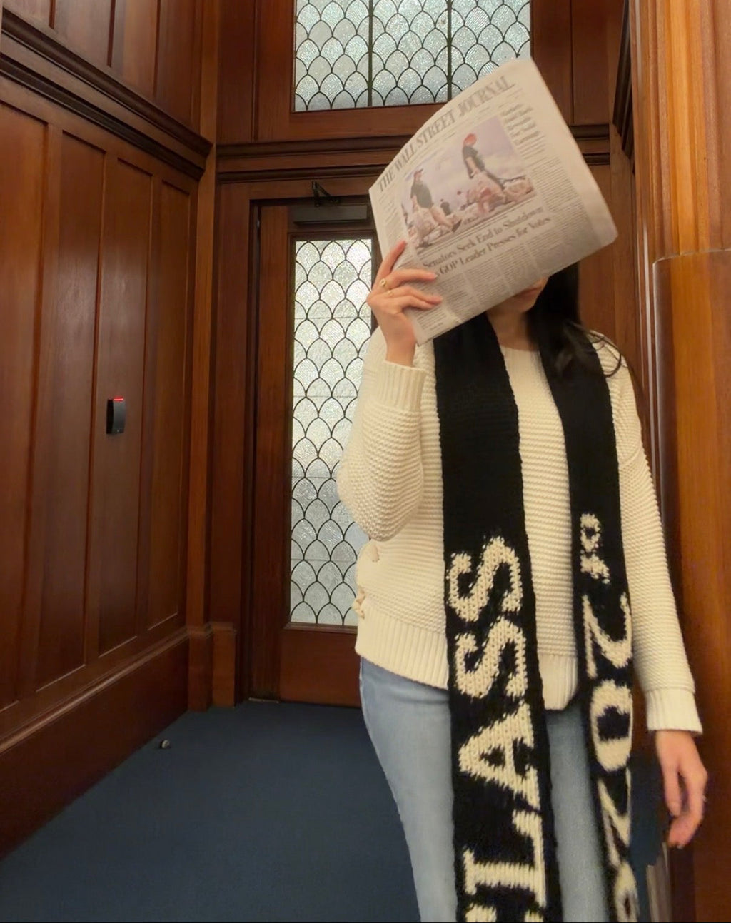 Person holding a book in front of their face in a wooden elevator with stained glass windows.