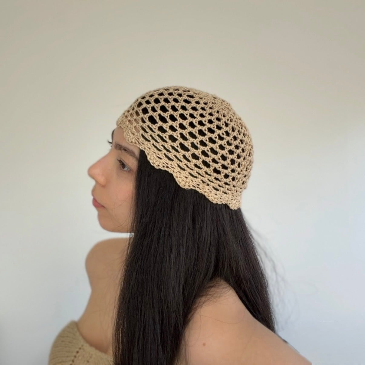 Woman wearing a beige knitted skull cap against a plain background